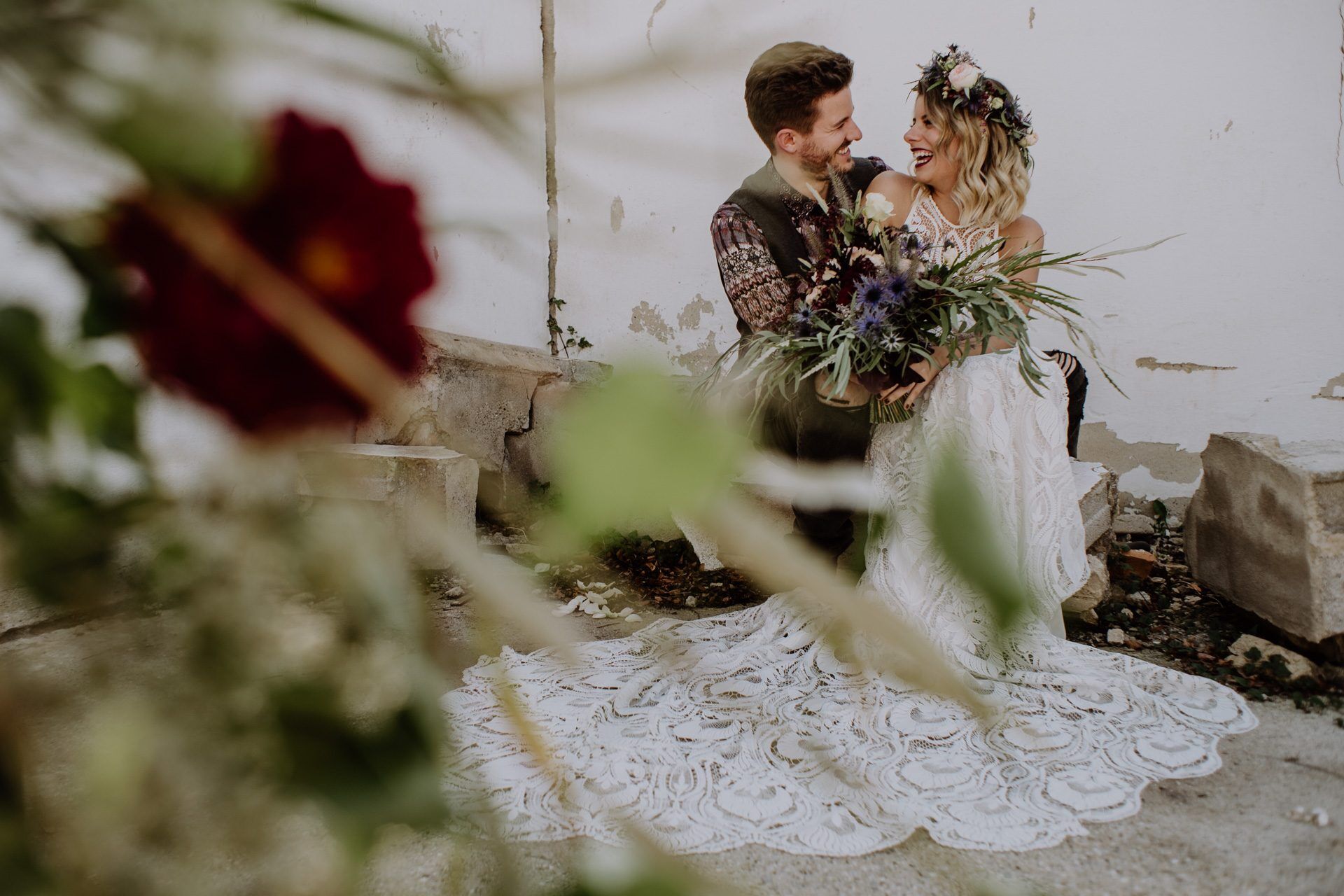 Braut mit wunderschönem Brautstrauß und Bräutigam lachen und sitzen auf einem Stein in einer alten Gärtnerei Hochzeit Hochzeitsideen Kamerakinder Weddings