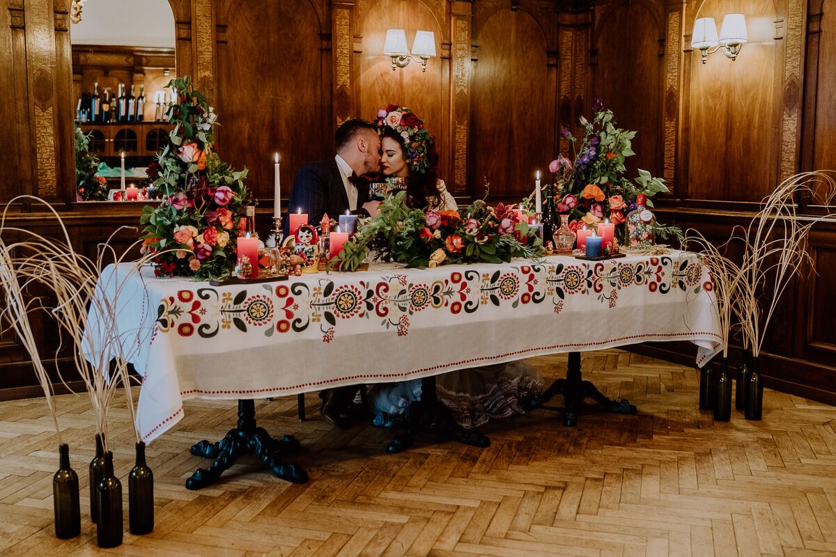 Hochzeitsinspiration Brautpaar sitzt am Brauttisch mit vielen Kerzen, viel bunter Dekoration und bohemian Flair und ganz viel Blumenschmuck boho Tischdekoration
