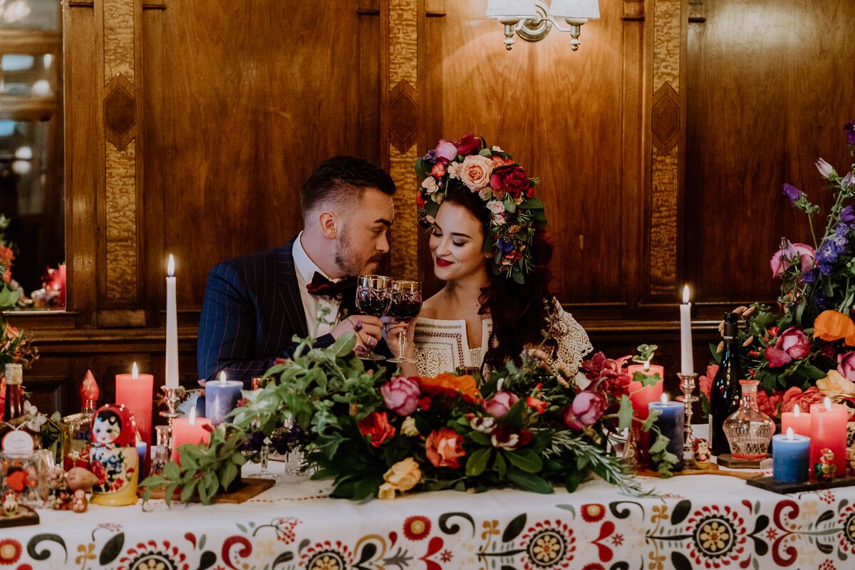 Hochzeitsinspiration Brautpaar sitzt am Brauttisch mit vielen Kerzen, viel bunter Dekoration und bohemian Flair und ganz viel Blumenschmuck boho Tischdekoration