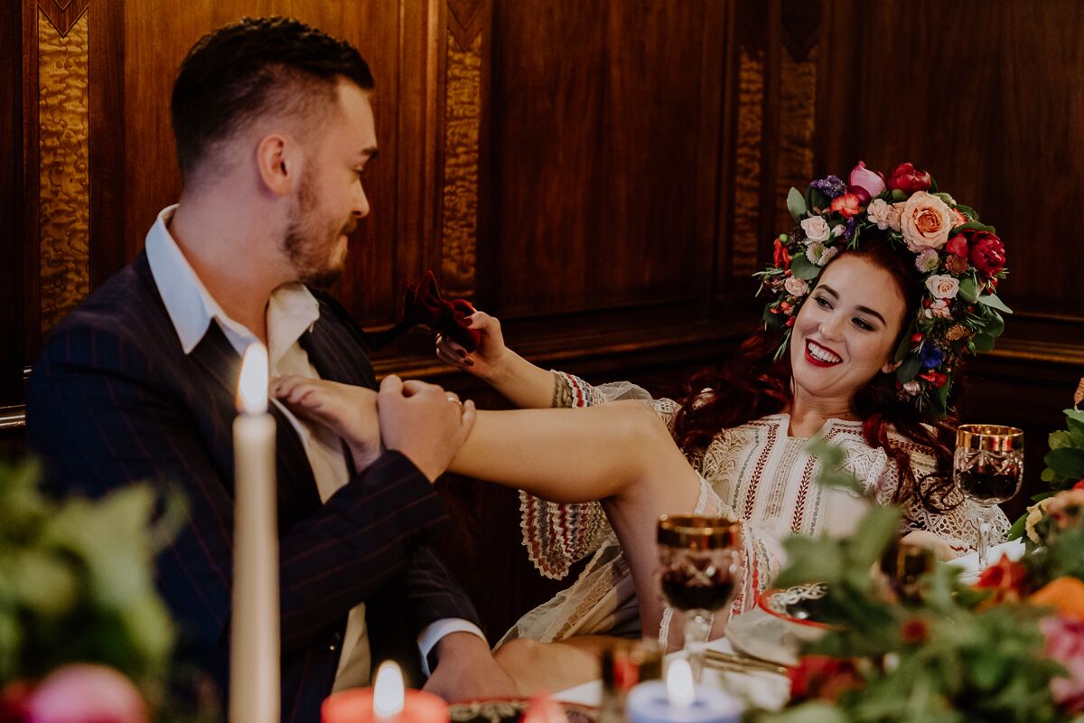 Hochzeitsinspiration Brautpaar sitzt am Brauttisch mit vielen Kerzen, viel bunter Dekoration und bohemian Flair und ganz viel Blumenschmuck boho Tischdekoration